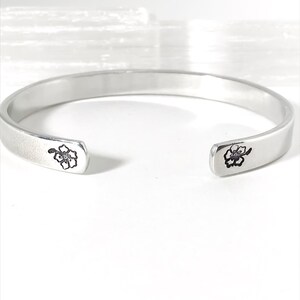 May include: A silver bangle bracelet with a delicate flower design on each end.