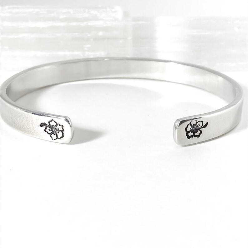 May include: A silver bangle bracelet with a delicate flower design on each end.