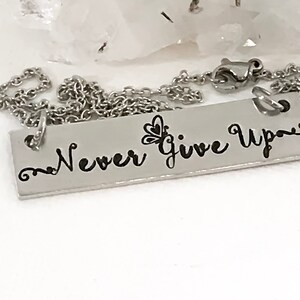 May include: Silver necklace with a rectangular pendant that says "Never Give Up" with a small butterfly design.