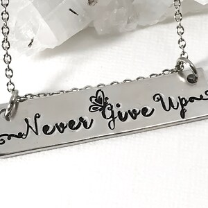 May include: A silver necklace with a rectangular pendant that reads "Never Give Up" with a small butterfly design.