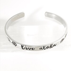May include: Silver bangle bracelet with the words "live aloha" engraved on it.