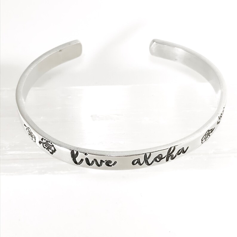 May include: Silver bangle bracelet with the words "live aloha" engraved on it.
