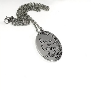May include: Silver necklace with an oval pendant that says "live love aloha" with a small heart between "live" and "love". The pendant is surrounded by a floral design.