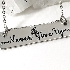 May include: Silver necklace with a rectangular pendant that says "Never Give Up" with a butterfly design.