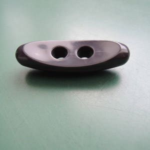 Könnte beinhalten: Ein schwarzer Plastikknopf mit zwei Löchern. Der Knopf ist oval geformt und hat eine glatte Oberfläche.