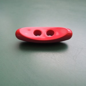 Könnte beinhalten: Ein roter Kunststoff-Toggle-Knopf mit zwei Löchern.