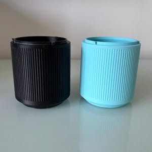 May include: Two cylindrical containers, one black and one light blue, with a ribbed texture. The containers are made of plastic and have a smooth, rounded bottom.