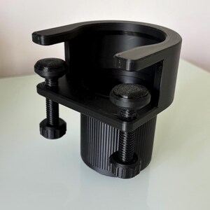 May include: Black plastic cup holder with two adjustable clamps. The holder has a threaded design and can be attached to a variety of surfaces.