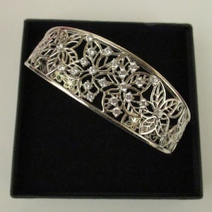May include: A silver bangle bracelet with a floral design and clear rhinestones.