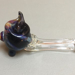 May include: A glass pipe with a clear stem and a colorful bowl. The bowl is made of dark blue glass with swirls of purple, yellow, and orange.