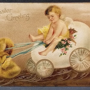 May include: An Easter greeting card featuring a cherub riding in a white egg-shaped carriage pulled by two yellow chicks. The cherub is wearing a yellow dress and a flower crown. The card has the text "Easter Greeting" in gold lettering.