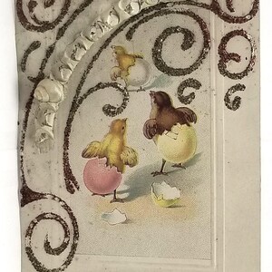 May include: A vintage Easter postcard featuring three yellow chicks hatching from eggs. The chicks are surrounded by a decorative border of swirls and glitter. The text "A Joyous Easter" is written in cursive at the bottom of the card.