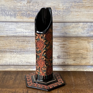 May include: Black wooden vase with a hexagonal base and a floral design in orange, green, and gold. The vase is decorated with a repeating pattern of flowers and leaves.