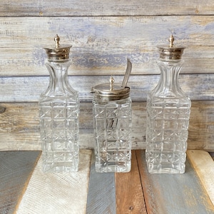 May include: Three clear glass bottles with silver tops and a textured pattern. The bottles are arranged in a row on a wooden surface.