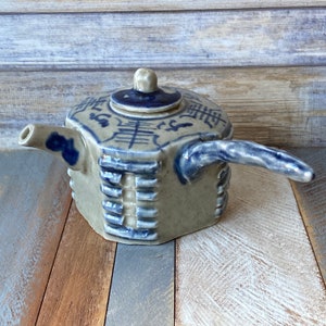 May include: A blue and white ceramic teapot with a unique octagonal shape and a textured design. The teapot has a spout and a handle, and it is decorated with Chinese characters.