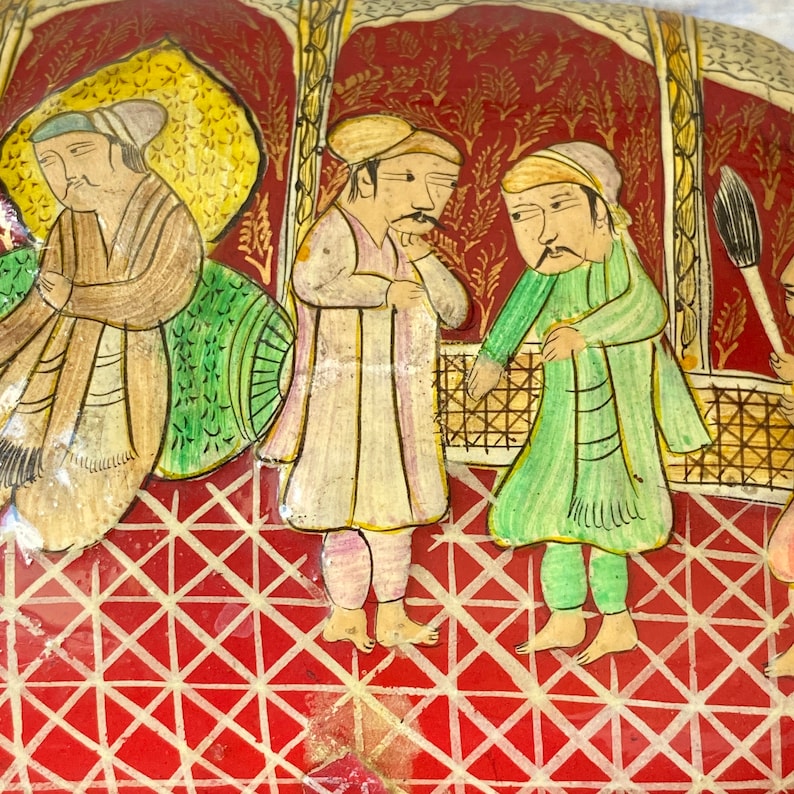 Op de afbeelding: Een handgeschilderd tafereel van mensen in traditionele kleding op een rode achtergrond met een wit geometrisch patroon. De sc&egrave;ne is geschilderd in een na&iuml;eve stijl met felle kleuren.