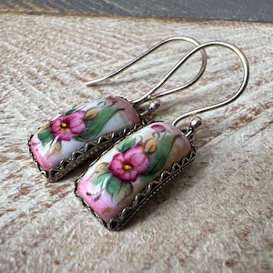 May include: A pair of silver dangle earrings with rectangular porcelain charms featuring hand-painted pink and green floral designs.