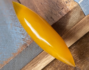 May include: A long, narrow, yellow, glossy, boat-shaped piece of amber.