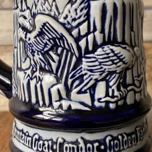 Pu&ograve; includere: Una boccale in ceramica blu e bianca con un design in rilievo di due condor in un ambiente montano. La boccale ha il testo "Mountain Goat Condor Golden Eagle" sul fondo.