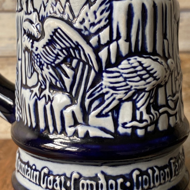 Pu&ograve; includere: Una boccale in ceramica blu e bianca con un design in rilievo di due condor in un ambiente montano. La boccale ha il testo "Mountain Goat Condor Golden Eagle" sul fondo.