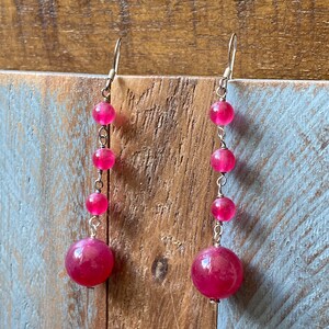 May include: A pair of long, dangling earrings with pink gemstone beads. The earrings are made of silver and have a simple design.