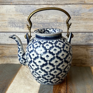 Könnte beinhalten: Eine blaue und weiße Porzellan-Teekanne mit einem Messinggriff. Die Teekanne hat ein Blumenmuster und ist mit einem geometrischen Design verziert.