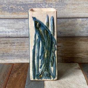 Op de afbeelding: Een witte keramische vaas met een abstract ontwerp in blauw en groen. Het ontwerp toont een gestileerde vis met een lange, vloeiende staart.