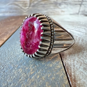Peut inclure: Une bague en argent avec une grande pierre précieuse de rubis de forme ovale. La bague a une bande texturée avec un motif décoratif.
