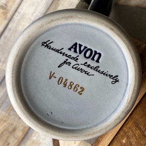 Pu&ograve; includere: Una tazza in ceramica bianca con una scritta blu e dorata che recita "AVON esclusivamente fatto a mano per Avon V-04862".