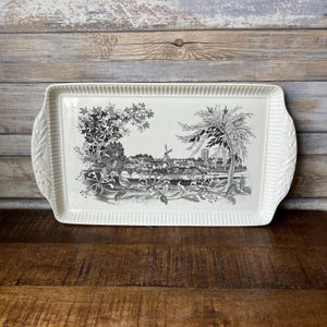 May include: A white ceramic serving tray with a black and white print of a town scene with a windmill. The tray has a raised edge and two handles.
