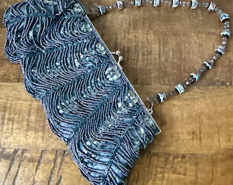 Puede incluir: Un bolso de noche vintage con cuentas en tonos turquesa y plata. El bolso presenta un patrón decorativo ondulado de cuentas y lentejuelas. El asa está hecha de pequeñas cuentas decorativas. El bolso está abierto, revelando el interior.