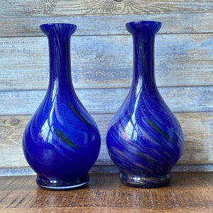 May include: Two blue glass vases with a swirling black and white pattern. The vases are tall and slender with a round base.