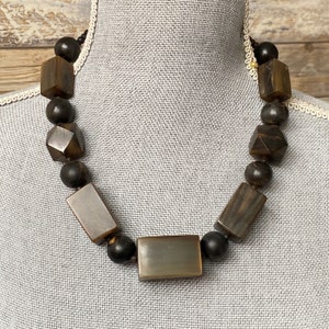 May include: A brown wooden necklace with large, geometric beads. The necklace is made of different shapes, including squares, rectangles, and diamonds.