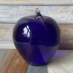 May include: A deep blue glass apple with a clear glass stem. The apple is smooth and reflective, and the stem is slightly curved.