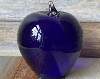 Op de afbeelding: Een donkerblauwe glazen appel met een heldere glazen steel. De appel is glad en reflecterend, en de steel is licht gebogen.