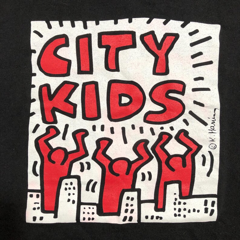 Puede incluir: Camiseta negra con un dise&ntilde;o gr&aacute;fico cuadrado blanco. El dise&ntilde;o presenta las palabras "CITY KIDS" en letras rojas, con tres figuras rojas con los brazos levantados sobre un paisaje urbano. El dise&ntilde;o es al estilo de Keith Haring.