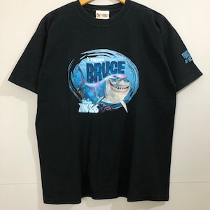 Op de afbeelding: Zwart T-shirt met een afbeelding van een haai met de tekst "I Found Bruce" en "Disney's Living Seas" op een blauwe en witte cirkel. De tekst "Friends of the Sea" staat op de rechtermouw.
