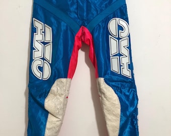 Op de afbeelding: Blauwe en roze motocrossbroek met witte letters die "F.I.S.C.O" op het linkerbeen en "C.I.F.S" op het rechterbeen zeggen. De broek heeft een witte riem en een wit label met de tekst "F.E.T. SPORTS CO."