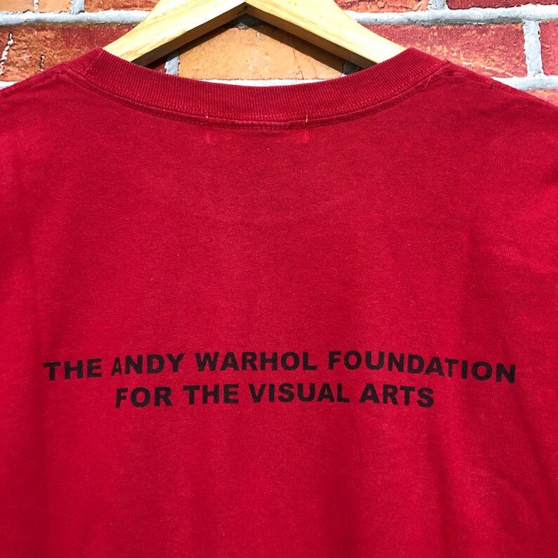 Puede incluir: Camiseta roja con el texto negro "THE ANDY WARHOL FOUNDATION FOR THE VISUAL ARTS". La camiseta tiene cuello redondo y est&aacute; hecha de una tela suave.