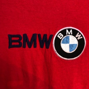 May include: Red fabric with the embroidered word "BMW" in navy blue and a circular BMW logo patch. The logo features a black border, white text, and a blue and white center.