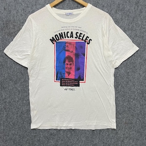 May include: White t-shirt featuring a graphic of Monica Seles with text that reads "Nothing can stop her now!" and "7th Grand Slam victory at FLUSHING MEADOW '92." The shirt also has the Yonex logo.