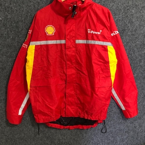 May include: Red and yellow Shell V-Power jacket with reflective stripes. The jacket has a high collar and a drawstring at the bottom. The Shell logo is on the left chest, and the V-Power logo is on the right chest.
