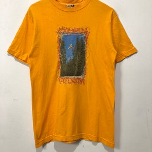 May include: A yellow t-shirt with a graphic print of a person snowboarding in a forest. The graphic is surrounded by a red and orange frame with the text "Bjorn Leines" and "Volcom" printed on it.