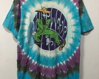 May include: A tie-dye t-shirt featuring a cartoon character wearing a hat and green suit. The character is sitting on a circle with the word "Widespread" written inside. The shirt is blue, purple and white.