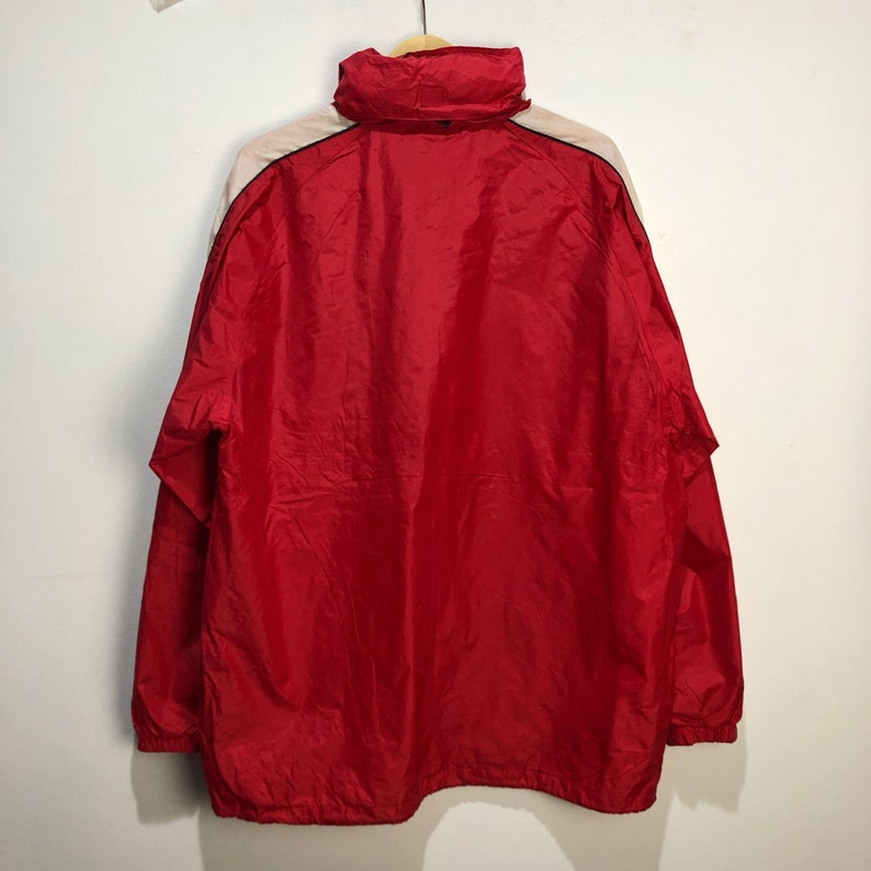 May include: A red windbreaker jacket with a white and black stripe down the sleeves. The jacket has a zipper closure and a hood.