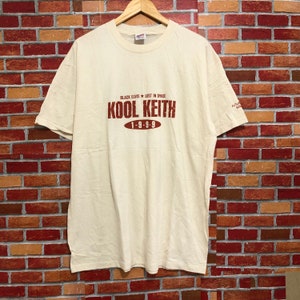 以下が含まれることがあります： 「Black Elvis * Lost in Space Kool Keith 1-9-9-9」と赤いグラフィックプリントが施されたヴィンテージの白いTシャツです。
