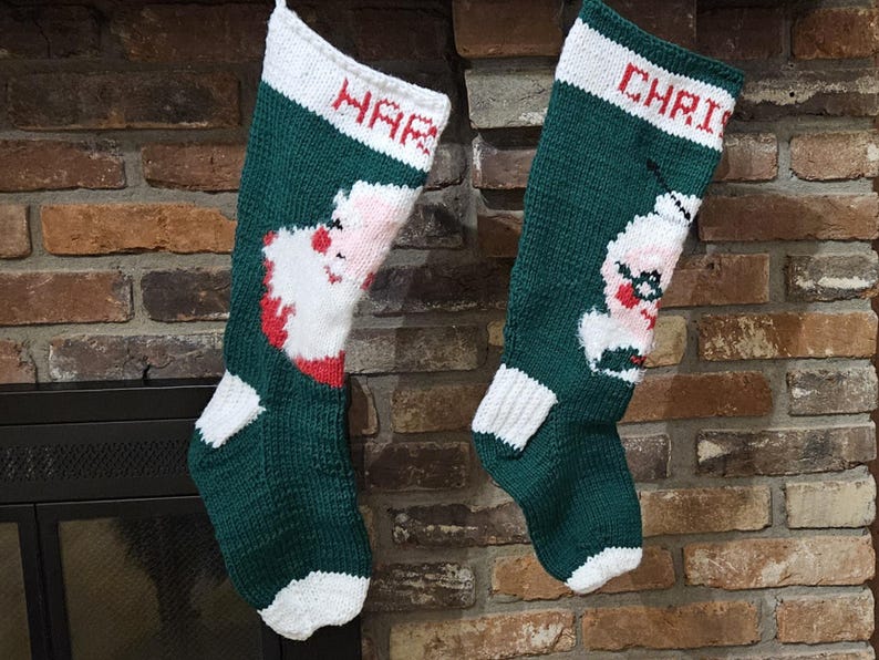 May include: Two green and white knitted Christmas stockings with Santa Claus designs. The stocking on the left says "Happy" and the stocking on the right says "Christmas".
