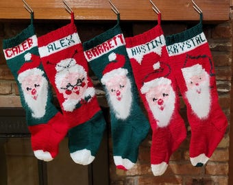 May include: Five personalised Christmas stockings with Santa Claus faces, each with a different name: Caleb, Alex, Barrett, Justin, and Krystal. The stockings are red and green with white trim.