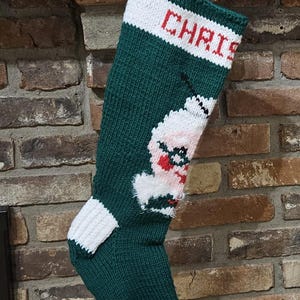 May include: Green knitted Christmas stocking with a white and red Santa Claus design and the name "Chris" embroidered in red on the cuff.