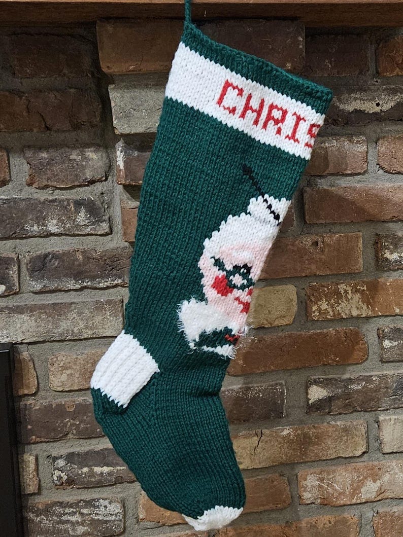 May include: Green knitted Christmas stocking with a white and red Santa Claus design and the name "Chris" embroidered in red on the cuff.